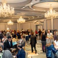 Wide scale shot of event space with many groups standing around the room and chatting